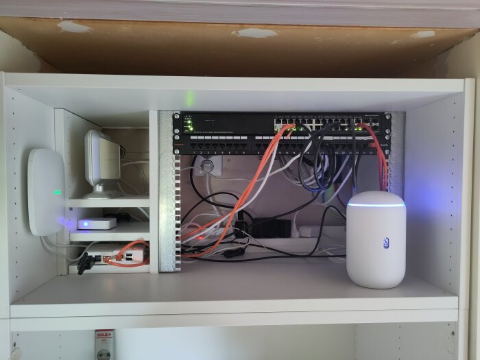 Nätverksskåp med switch, router, kablar och patchpanel i ett hem eller litet kontor.