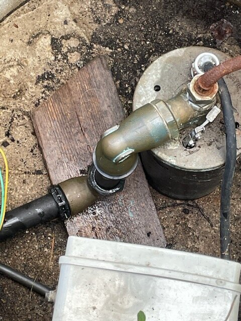 Rörkonstruktion på marken med elektriska ledningar, betong, träbit och metallbehållare. Reparation eller underhållsarbete verkar pågå.