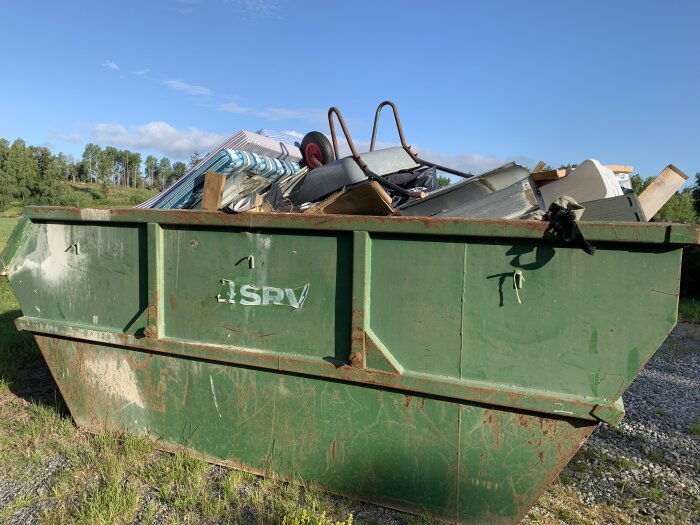 Grön container överfull med skräp utomhus under klar himmel.