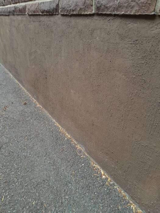 Brun vägg och trottoar, viss löv, subtil textur, murbruk, linjens spel.