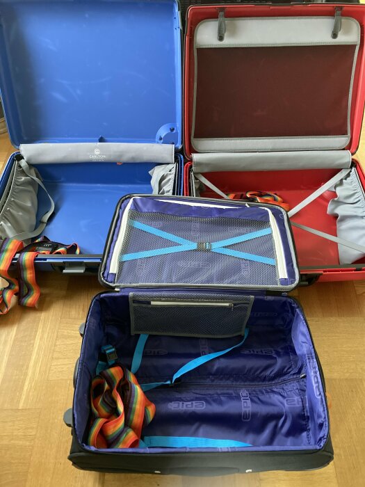 Tre öppna resväskor med färgglada band, ordning inför packning på trägolv.