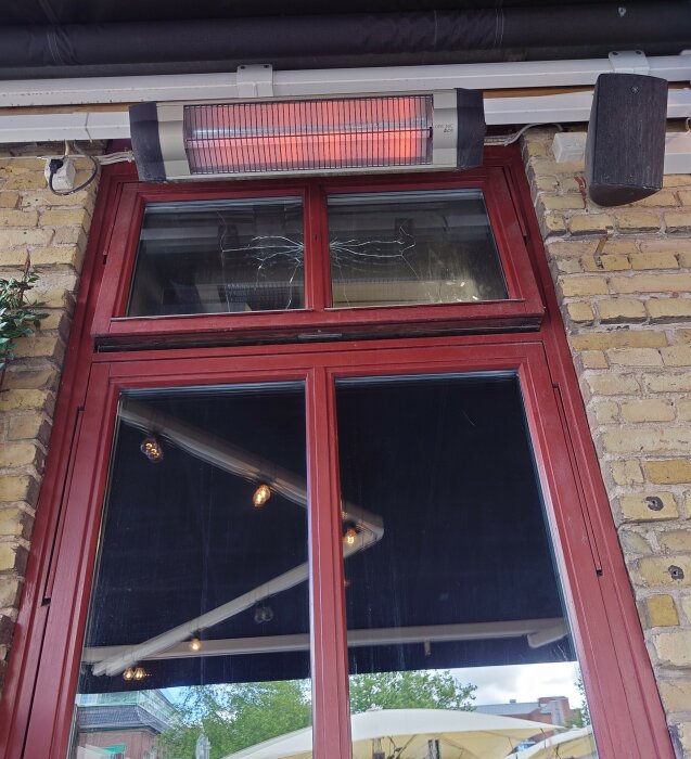 Röd fönsterram, infravärmare, högtalare, tegelvägg, reflektion av lampor i glaset.