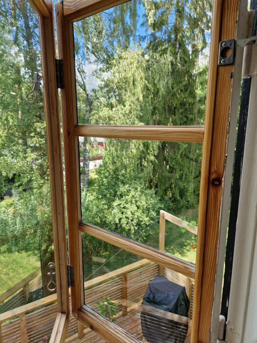 Öppet fönster med utsikt över gröna träd och en träaltan under sommaren.