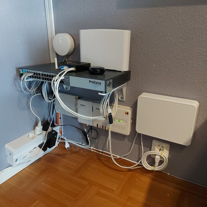 Nätverksutrustning på väggen inklusive switch, router, kablar och trådlösa åtkomstpunkter. Anordnat oorganiserat.