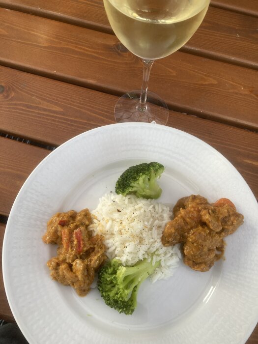 Vitt ris, broccoli, gryta, vitvinsglas, träbord. Måltid utomhus.