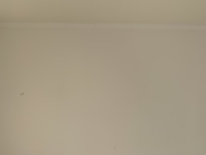 En off-white vägg möter taklisten i ett tomt rum. Minimalistisk, monokrom, lugnande och sparsmakad i detaljer.
