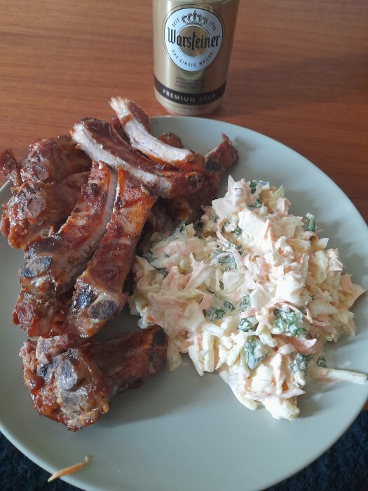 Grillade revbensspjäll, potatissallad, Warsteiner-ölflaska. Måltid på träbord.
