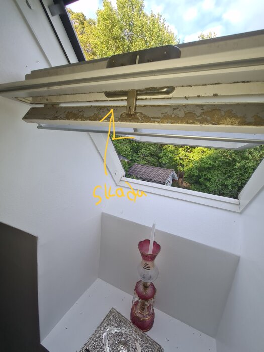 Ett öppet fönster i taket med synlig mögel, trädet utsikten, inomhus hörn med ljusstake och bordstablett.