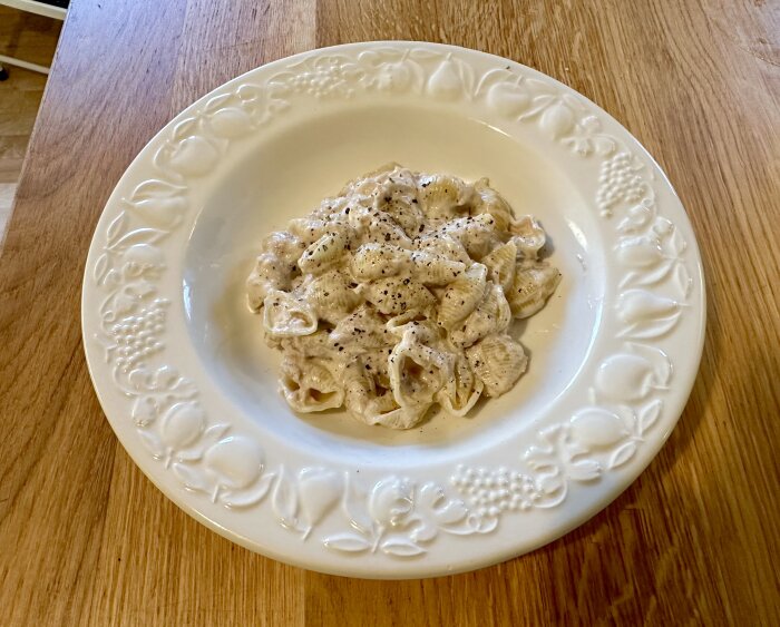 En tallrik pasta med krämig sås och svartpeppar på ett träbord.