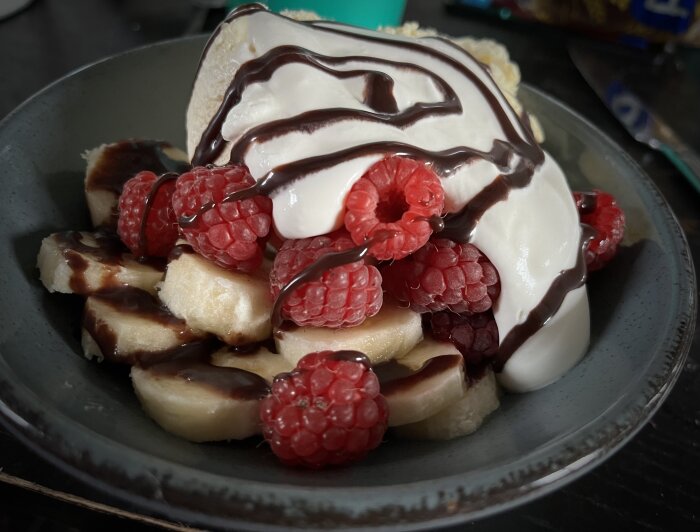 En skål med glass, banan, hallon och chokladsås. En söt dessert.