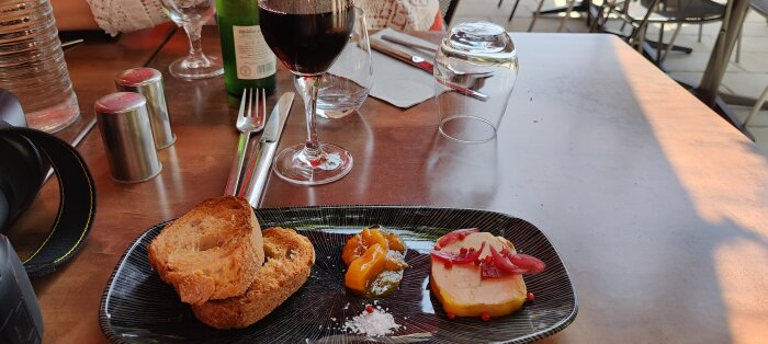 Ett cafébord utomhus med vin, bröd och paté. Avslappnad stämning, matupplevelse vid solnedgång.