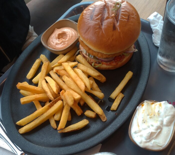 Hamburgare med pommes och såser på svart bricka, rykande mat, vardagsmåltid.