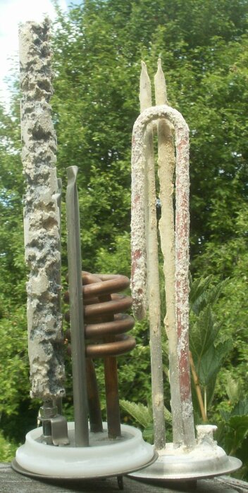 Gamla, använda ljusstumpar står på ljusstake utomhus mot gröna träd i bakgrunden. Slitna, övergivna, vaxrester.