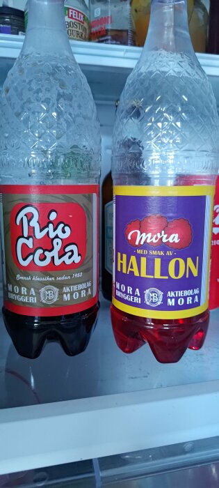 Två läskflaskor i ett kylskåp, etiketterna liknar kända dryckesmärken, möjligen parodier.