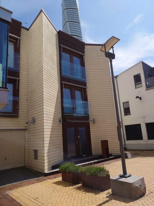 Modernt hus med träpaneler, dörr, fönster, planteringslåda, gatlykta, kullersten, Turning Torso i bakgrunden.