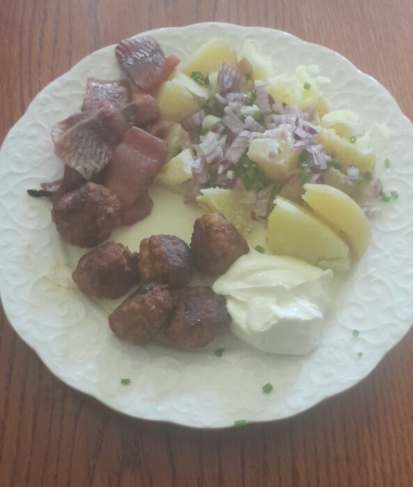 Ett måltid med köttbullar, potatis, gräddfil, rödlök och bacon på en vit tallrik.