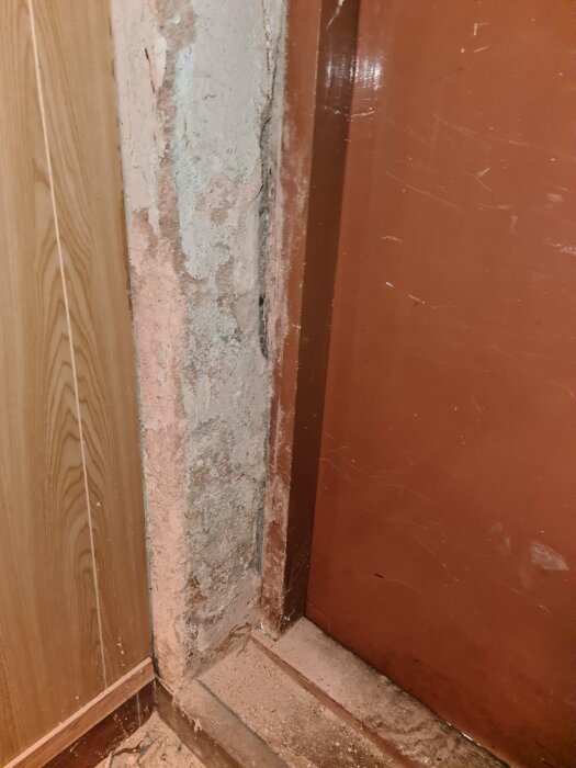 Slitet hörn med avskalad färg och synlig betong vid en dörrpost, behöver renovering.