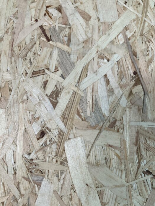 En närbild på spånskiva eller OSB (oriented strand board) som visar texturerade träflisor komprimerade tillsammans.