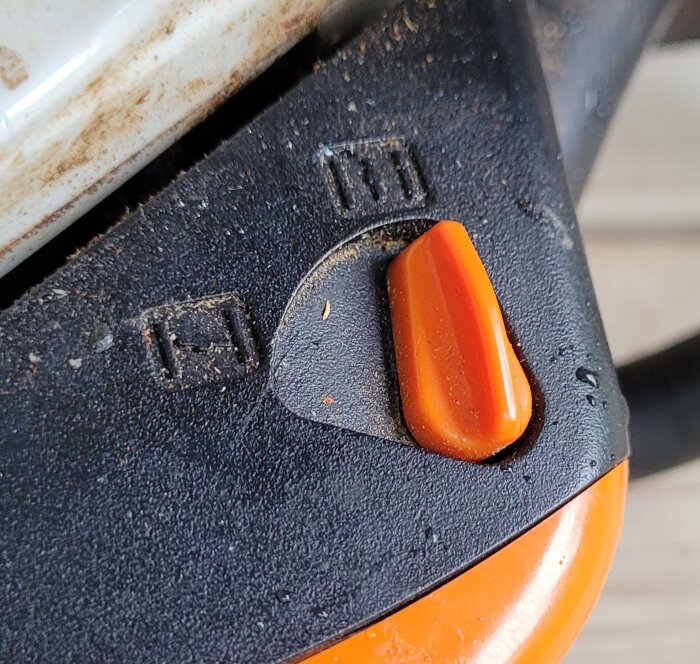 Närbild på en smutsig strömbrytare med orange knapp på en apparat. Slitage och damm.