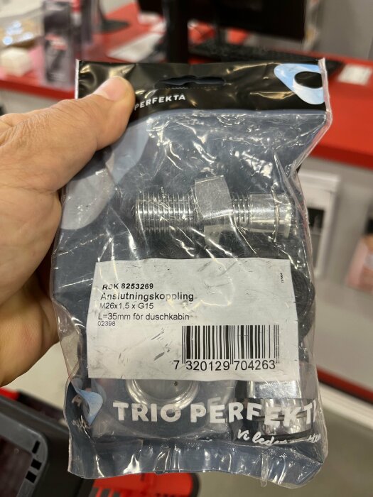 En hand håller en förpackning med en metallisk anslutningskoppling märkt "Trio Perfekta" för duschinstallation.