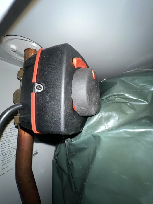 Närbild av en svart och röd enhet, troligen ventilationsutrustning, med kopparledningar och skyddande grön plast.