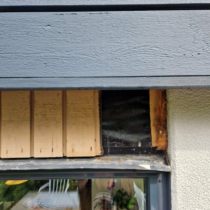 Fönster med skador på ytterpanel och isolering synlig, tecken på byggnadens underhållsbehov.