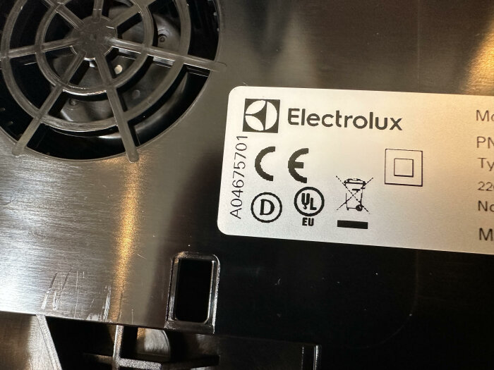 Etikett av Electrolux med säkerhetssymboler och serienummer, nära en spisbrännare.