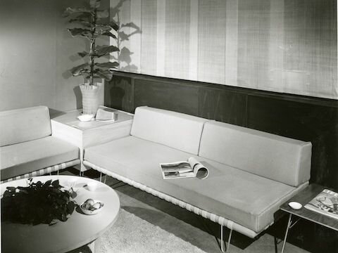 Svartvitt foto av retro vardagsrum, minimalistiska möbler, soffa, fåtölj, soffbord, tidskrifter, planta, enkel design.