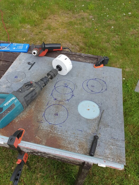 Arbetsbord med verktyg, hålsåg, borr och utmarkerade punkter på metallplåt, utomhus verkstadsprojekt.