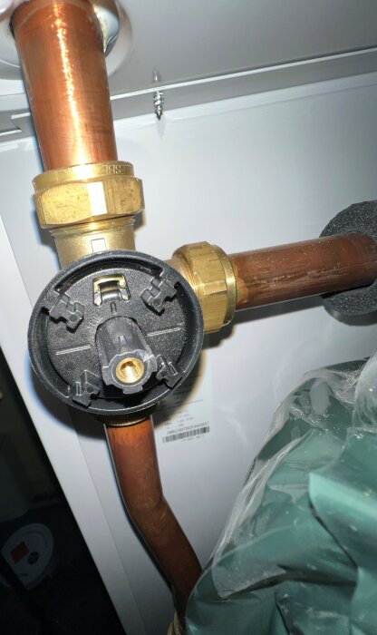 Röranslutning med svart plastlock och mässingskopplingar mot vit bakgrund, inomhus VVS-installation.