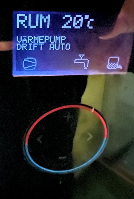 Digital display visar rumstemperatur 20°C, värmepump i automatläge, otydligt rött och blått föremål nedanför.