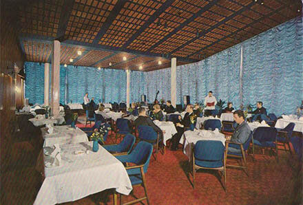 Restauranginteriör med retrostil, blå stolar, vita dukar, serveringspersonal och middagsgäster. Tidstypisk design, möjligen mitten av seklet.