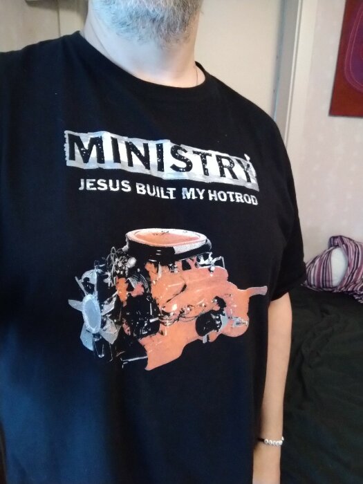 Person i svart t-shirt med text och bild av motor. Stiliserad grafik och text: "MINISTRY JESUS BUILT MY HOTROD".