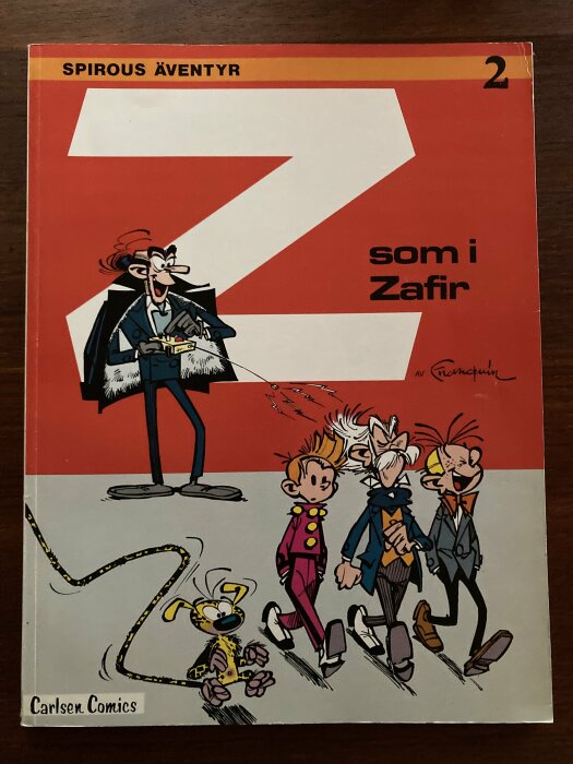 Seriealbumomslag, "Spirous Äventyr 2", tecknade figurer, röd bakgrund, titel "Z som i Zafir", Carlsen Comics.