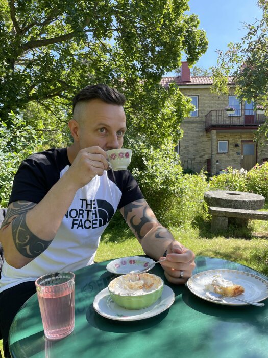 Man dricker kaffe utomhus vid ett grönt bord med matrester och ett glas saft.