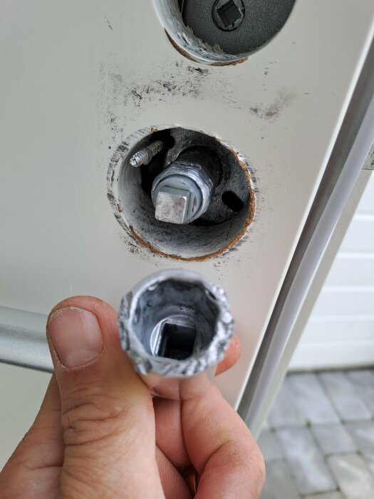 En hand håller en avbruten låskolv nära en dörr med utborrade låshus.