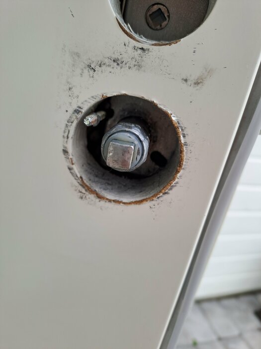 Närbild av en skadad dörr med en bult och skruv genom rostig öppning.