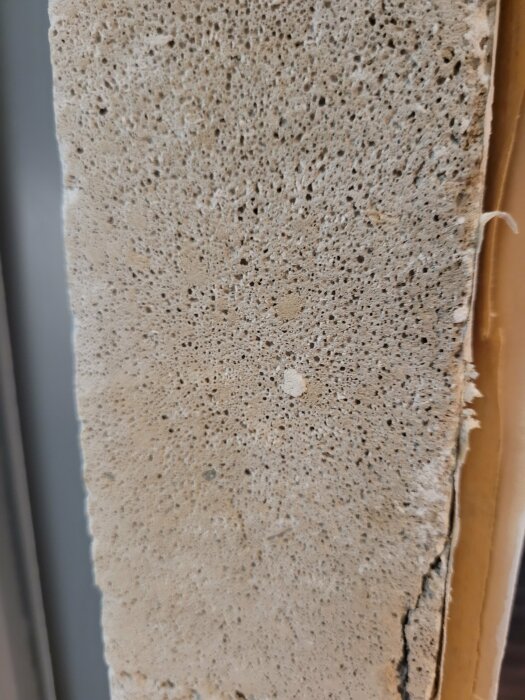 Närbild på sliten, porös yta av en betongvägg eller panel med tydliga hål och sprickor.