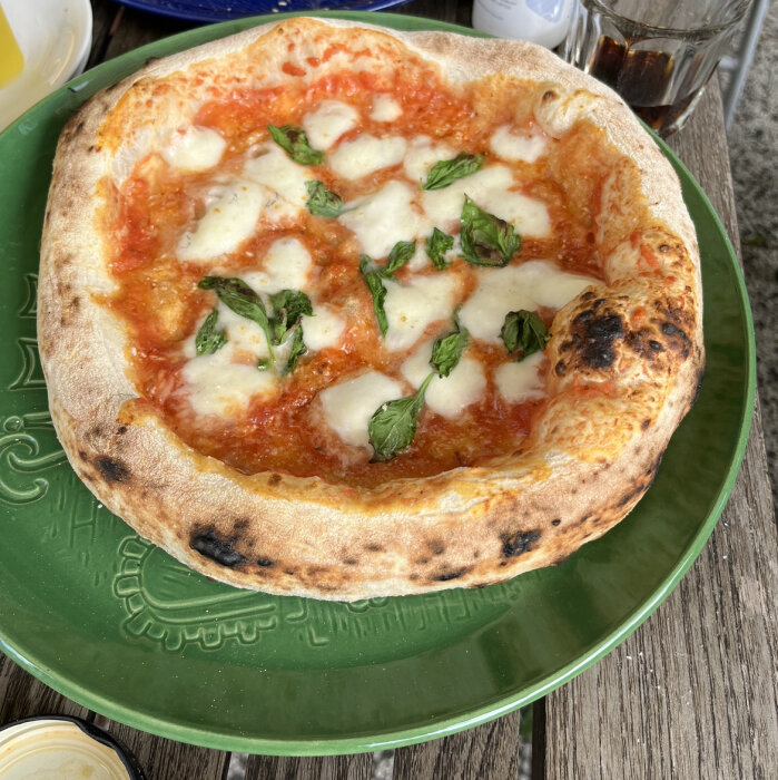 Nybakad pizza Margherita med tomatsås, mozzarella och basilika på grönt fat.