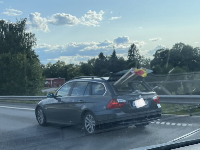 Bil med öppet baklucka transportera stora föremål på motorväg, ljust väder, något oskarp bild.