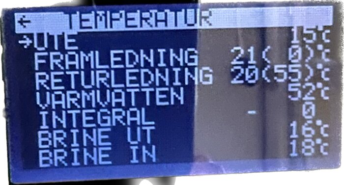 Digital display visar temperaturdata för värmepump eller värmesystem med numeriska värden och bokstäver, suddig bakgrund.