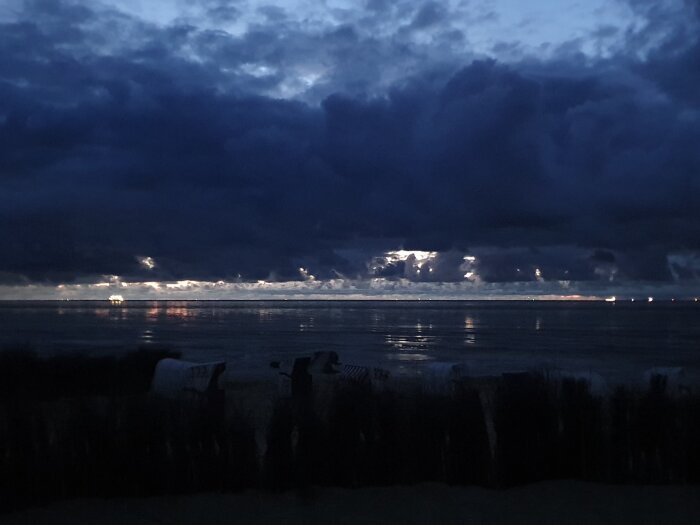 Mörk himmel, moln, kvällsljus reflekterar på hav, sikt av kusten, lugn, dramatisk natur, dygnets skymning.