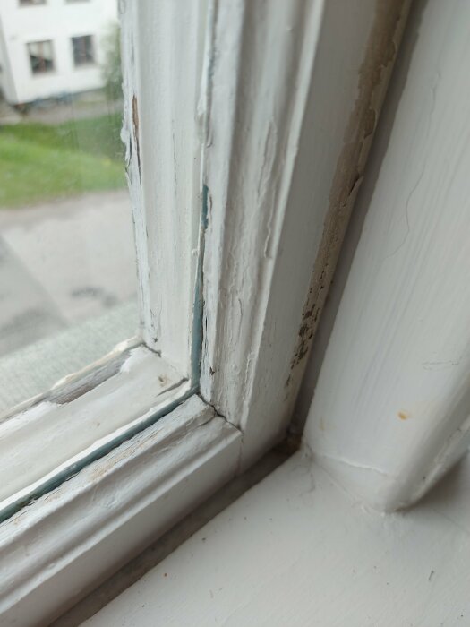 Slitet fönsterkarmshörn med flagande färg och synlig sprickbildning vid fönsterglaset. Behov av underhåll eller renovering.