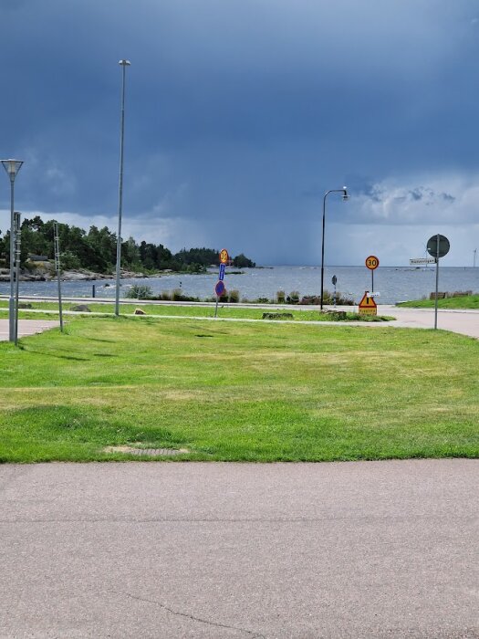 Gräsmatta, vägskyltar, molnig himmel, havsutsikt, gatlyktor, öde landskap.