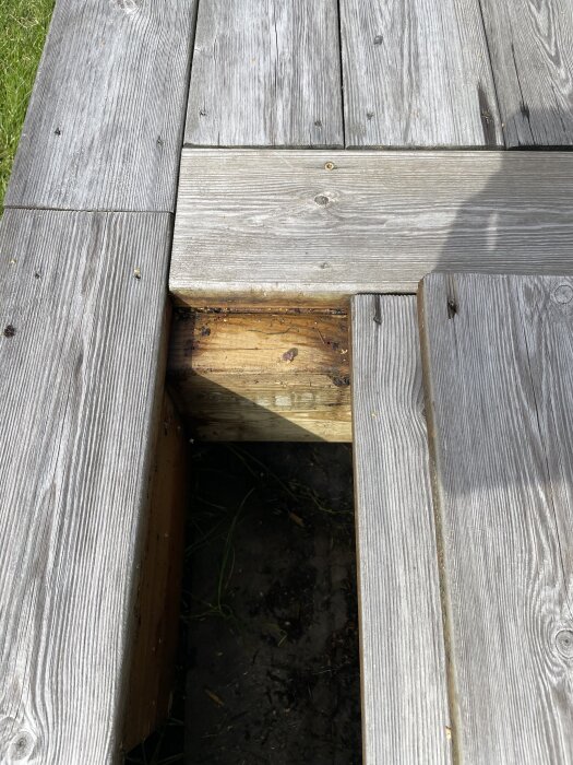 Trätrall utomhus med saknat bräde, visar underliggande mörk jord.