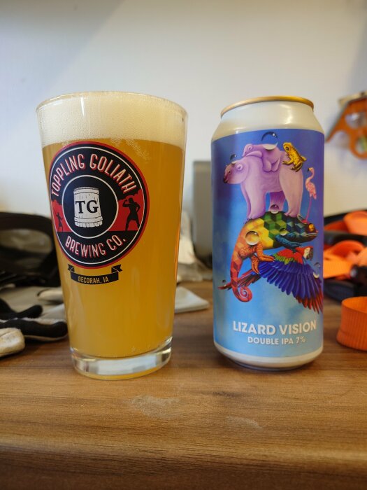 Ett glas öl bredvid en ölburk med färgrik etikett, "Lizard Vision Double IPA," på bord.