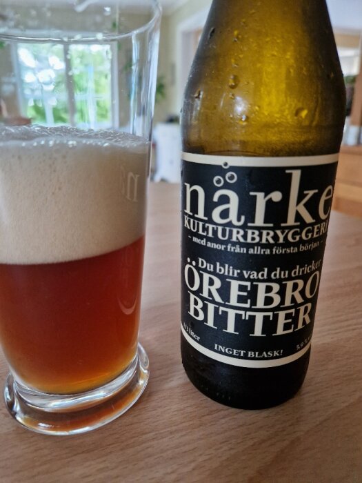 Ölglas med skum, flaska från Närke Kulturbryggeri, Örebro Bitter, transparent bakgrund, inomhusmiljö.