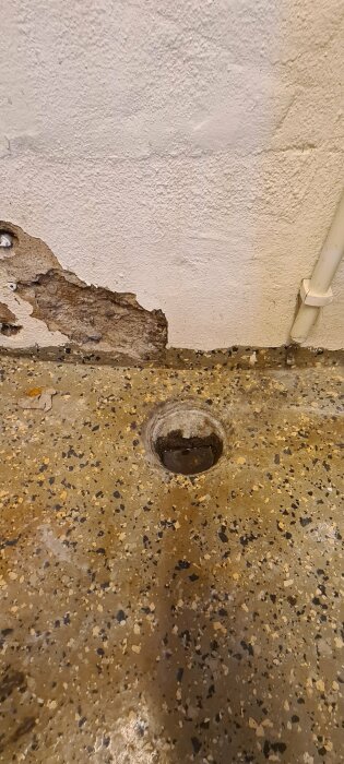 Vattenavlopp i betonggolv, skadad vägg, rörsystem, behov av underhåll eller reparation.