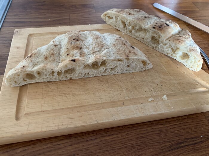 Skivat, luftigt bröd på träskärbräda, bakgrunden en bänkskiva, synlig knivskärning, enkel hemlagad måltid.