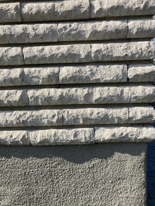 En vägg med stenblock skapar skuggspel på betong under klarblå himmel.